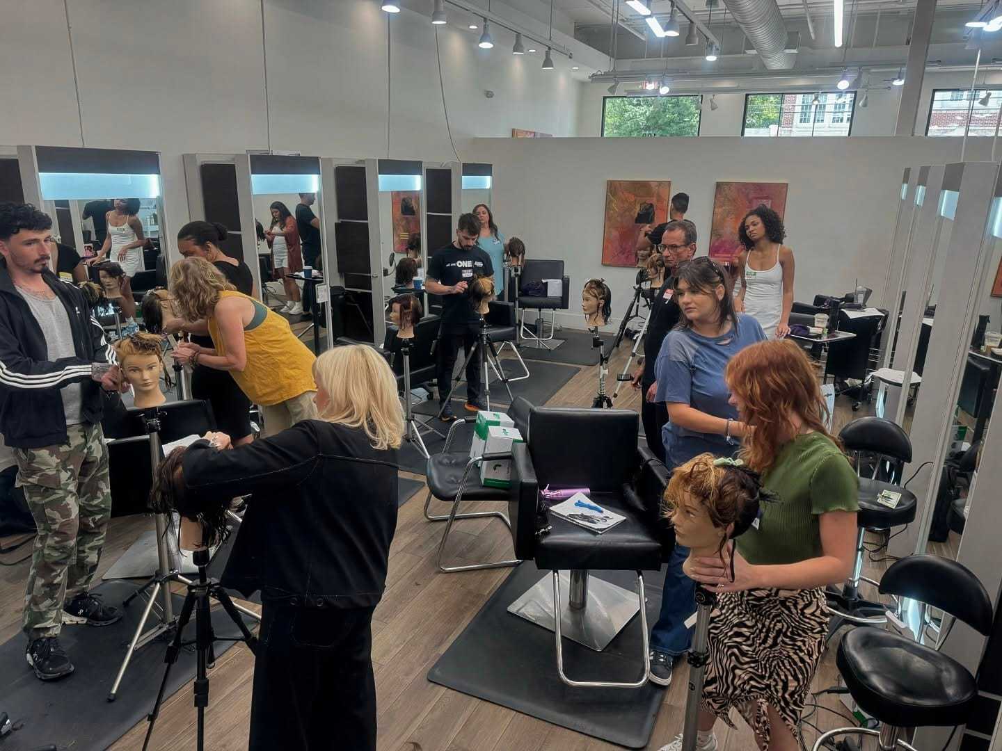 Hairdressing class with students practicing on mannequins in a well-lit salon.